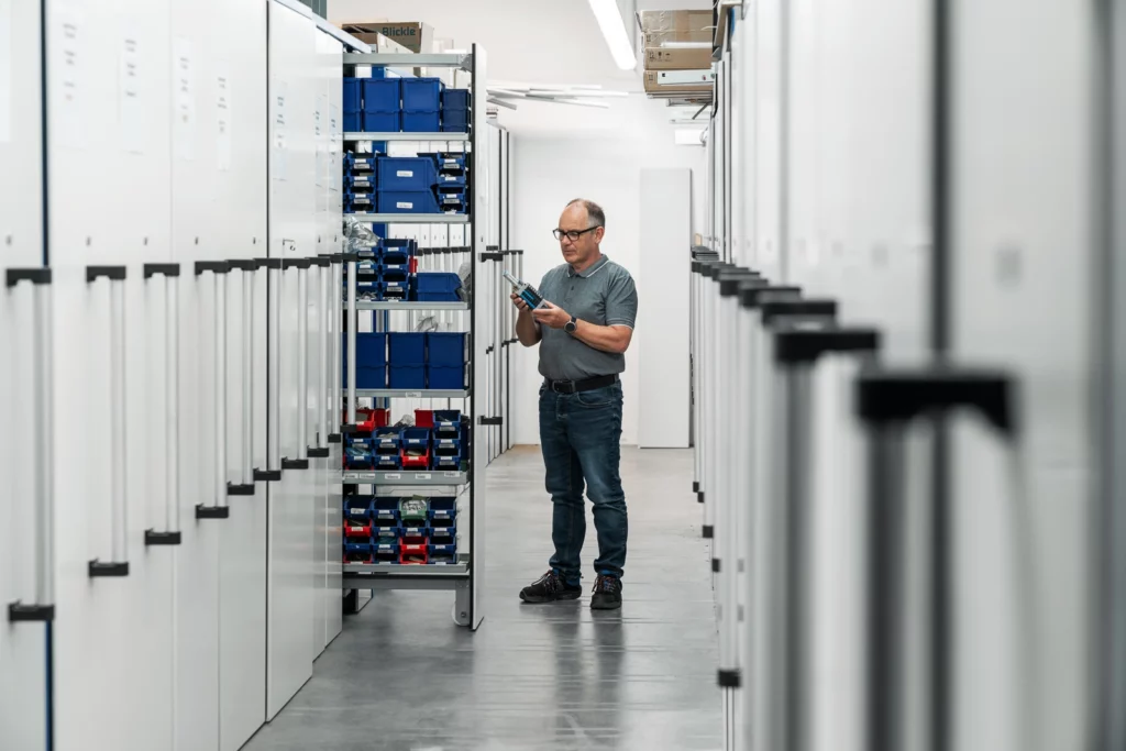 Mann steht in Archiv und hält ein Produkt in der Hand